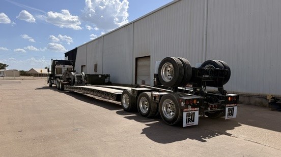 Multi-axle lowboy trailer with flip axle parked beside a building