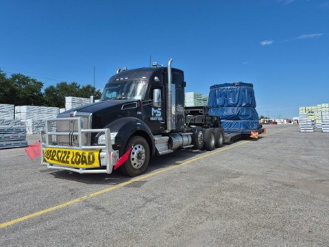 Kenworth with oversize banner and a tarped load on a lowboy